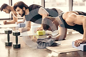 handsome sportsmen simultaneously doing plank and using blocks