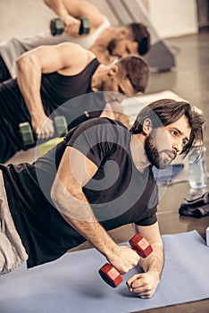 handsome sportsmen simultaneously training with dumbbells on floor