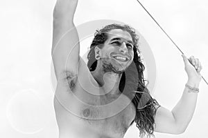 A handsome sporty guy with long hair smiling against a blue clear sky with white clouds. Journey on a yacht by sea. Travel im
