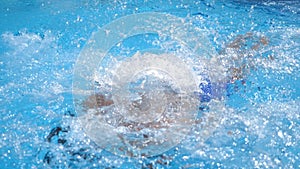 Handsome sporty man floating across pool with clear blue water. Young guy swimming and enjoying recreation on resort in