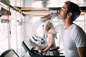 Handsome sporty man resting, having break drinking water after doing exercise