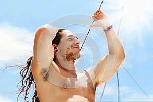 A handsome sporty guy with long hair against a blue clear sky with white clouds. Journey on a yacht by sea. Travel image.