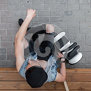 Handsome sporty young man sitting on a wooden step next to a modern white hoverboard. Top view on fashionable guy