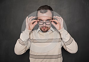 Handsome strict teacher in eyeglasses looking at you on blackboard