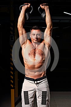 Handsome strong man doing the exercises with kettlebells in sportwear shorts on dark shadow background. Closeup bright portrait. photo