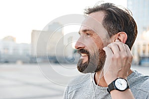 Handsome strong mature sportsman listening music with earphones.
