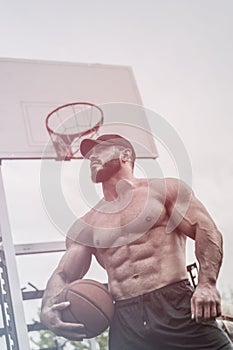 Handsome strong young muscular caucasian male with beard holding basketball ball on backboard backgroung