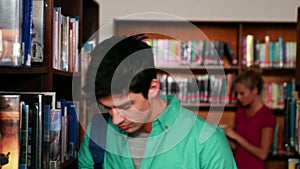 Handsome student picking out a book in the library