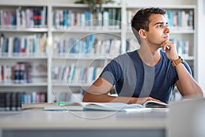 Handsome student reading a book for his class in a bright modern library