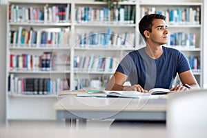 Handsome student reading a book for his class in a library