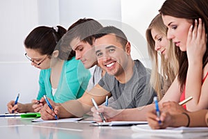 Handsome student sitting with classmates writing at desk