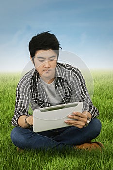 Handsome student uses tablet at field