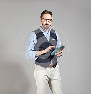 Handsome stylish bearded man in classic vest holding tablet