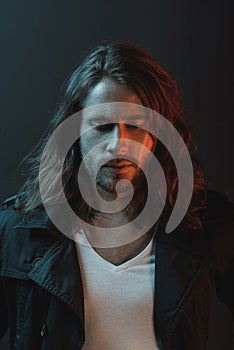 Handsome stylish bearded young man with long hair looking down in studio