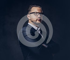 Handsome stylish businessman with serious face in an elegant formal suit standing with crossed arms. Isolated on a dark