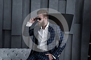 Handsome stylish man in blue suit in a cage and eyewear at home sitting on sofa