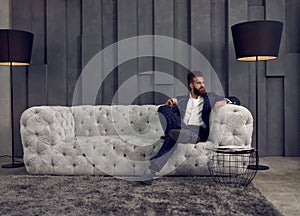 Handsome stylish man in blue suit in a cage at home sitting on sofa