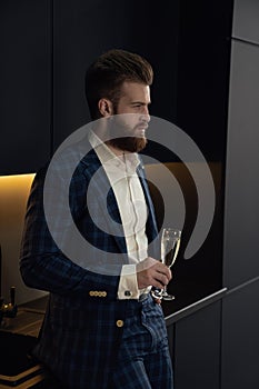 Handsome stylish man in blue suit in cage at home. Standing in modern black kitchen with glass of champagne