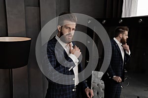 Handsome stylish man in blue suit in a cage at home standing on sofa near mirror. Holds his chin