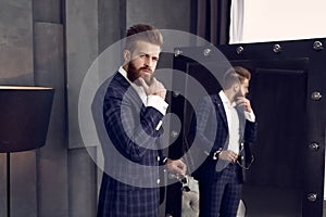 Handsome stylish man in blue suit in a cage at home standing on sofa near mirror. Holds his chin