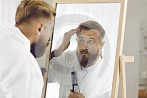 Handsome stylish man combing and styling his hair in morning in front of mirror.