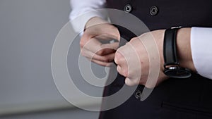 Handsome stylish man dressed in modern formal clothes buttoning jacket. Close up of hands of guy in blue jacket, white