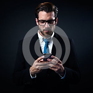 Handsome stylish man in elegant black suit using mobile phone.