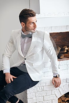 Handsome stylish man in elegant suit sitting near fireplace