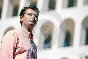 Handsome stylish man outdoors, with striped shirt. Sunglasses not worn. Building in the background