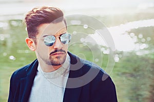 Handsome stylish man with sunglasses and modern hairstyle and beard. Outdoor in the street.