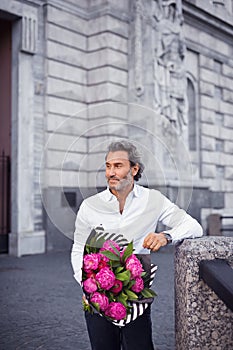 A handsome stylish man in a white shirt and black trousers and a bouquet of peonies in his hands