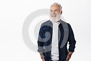 Handsome stylish old hipster man, senior with white beard and tattoos, looking aside at advertisement with pleased face