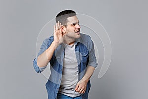 Handsome stylish unshaven young man in denim jeans shirt posing isolated on grey wall background studio portrait. People