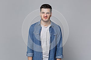 Handsome stylish unshaven young man in denim jeans shirt posing isolated on grey wall background studio portrait. People