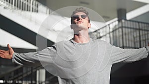 Handsome stylish white man in sunglasses raises his hands sides background city street. Tough confident guy Motivation and freedom