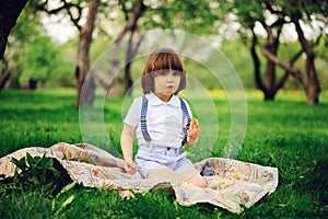 Handsome stylish 3 years old toddler child boy with funny face in suspenders enjoying sweets on picnic