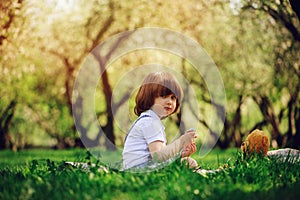 Handsome stylish 3 years old toddler child boy with funny face in suspenders enjoying sweets on picnic in spring