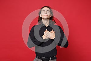 Handsome stylish young curly long haired man in black shirt posing isolated on red wall background studio portrait