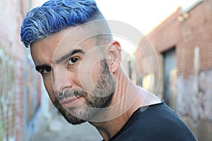 Handsome stylish young man with artificially colored blue dyed hair undercut hairstyle, beard and piercings with copy space