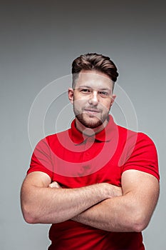 Handsome successful smiling young guy businessman with arms crossed, stylish haircut, studio portrait on gray background