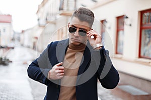 Handsome successful young businessman in an elegant coat with silver clock in sunglasses in a knitted warm sweater