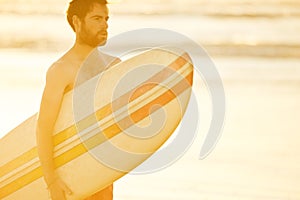 Handsome surfer holding a surfboard under his arm on beach