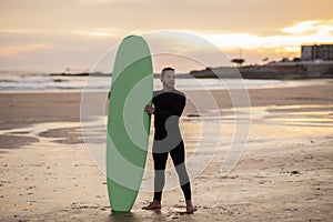 Handsome Surfer Man With His Surfboard Standing On The Beach At Sunset