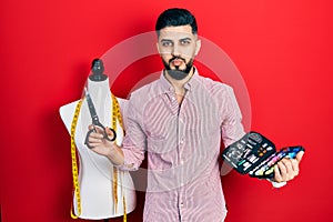 Handsome tailor man with beard holding sew kit and scissors looking at the camera blowing a kiss being lovely and sexy