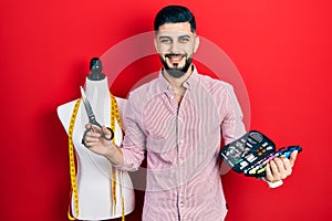 Handsome tailor man with beard holding sew kit and scissors smiling and laughing hard out loud because funny crazy joke