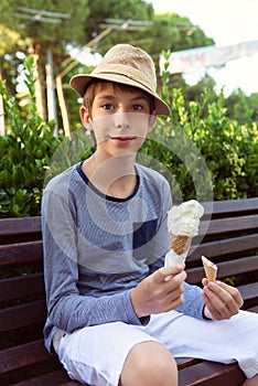 Handsome teen boy eating ice cream, summer outdoor. 12 years old cheerful boy with hat holding ice-cream