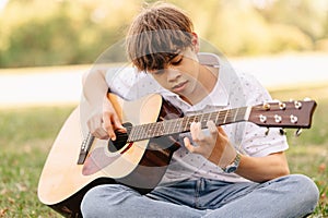 Handsome teen boy is learning how to play guitar while sitting in park.