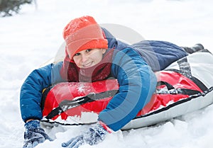 Handsome teen laughing and showing excitement while he slides downhill. snow tubing on winter day outdoors.