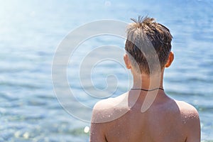 handsome teenage boy on the beach in a swimsuit looks at the sea. Attractive young man on the background of the sea.