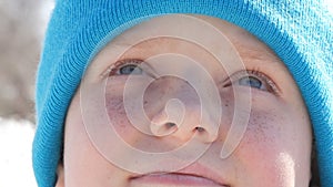 A handsome teenager boy with blue eyes, lots of freckles on his face and a cap in the tone of his eyes, looks up on the